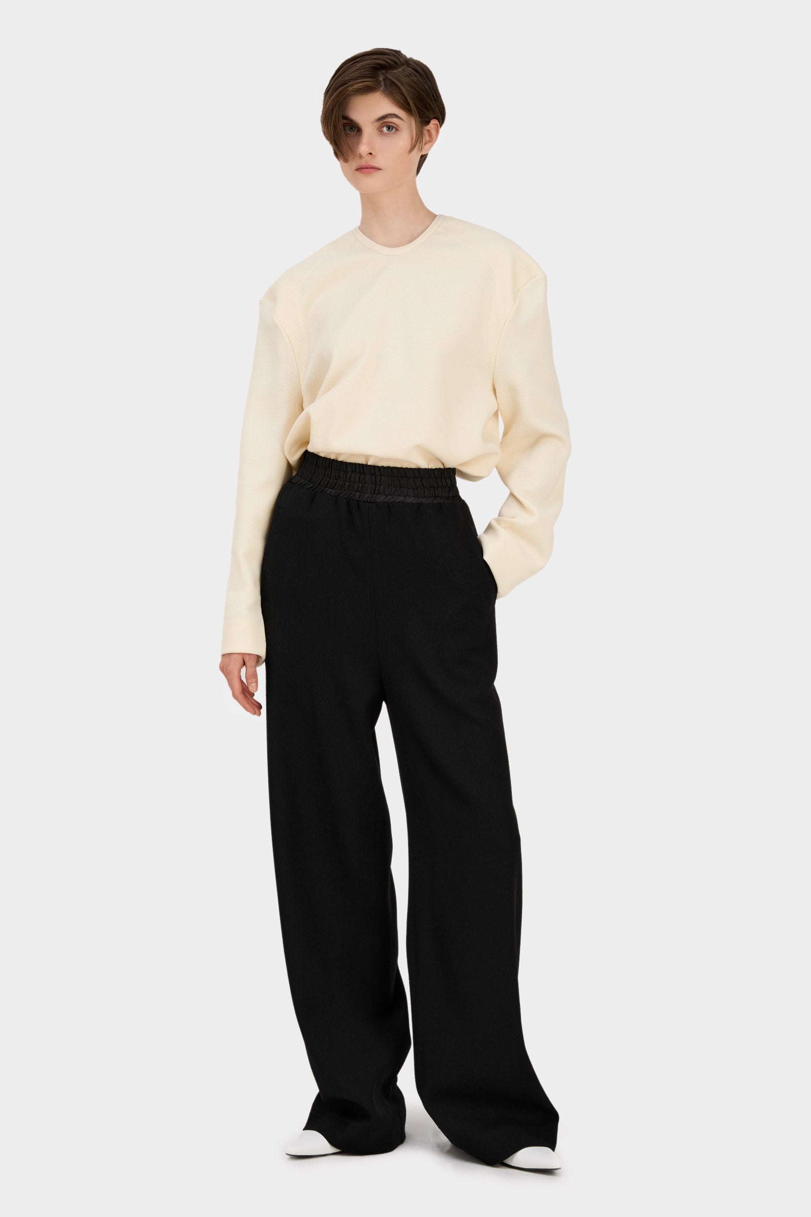A model wearing black wool pants SOUL PANTS BLACK and a beige knit top, standing against a plain background.