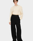A model wearing black wool pants SOUL PANTS BLACK and a beige knit top, standing against a plain background.