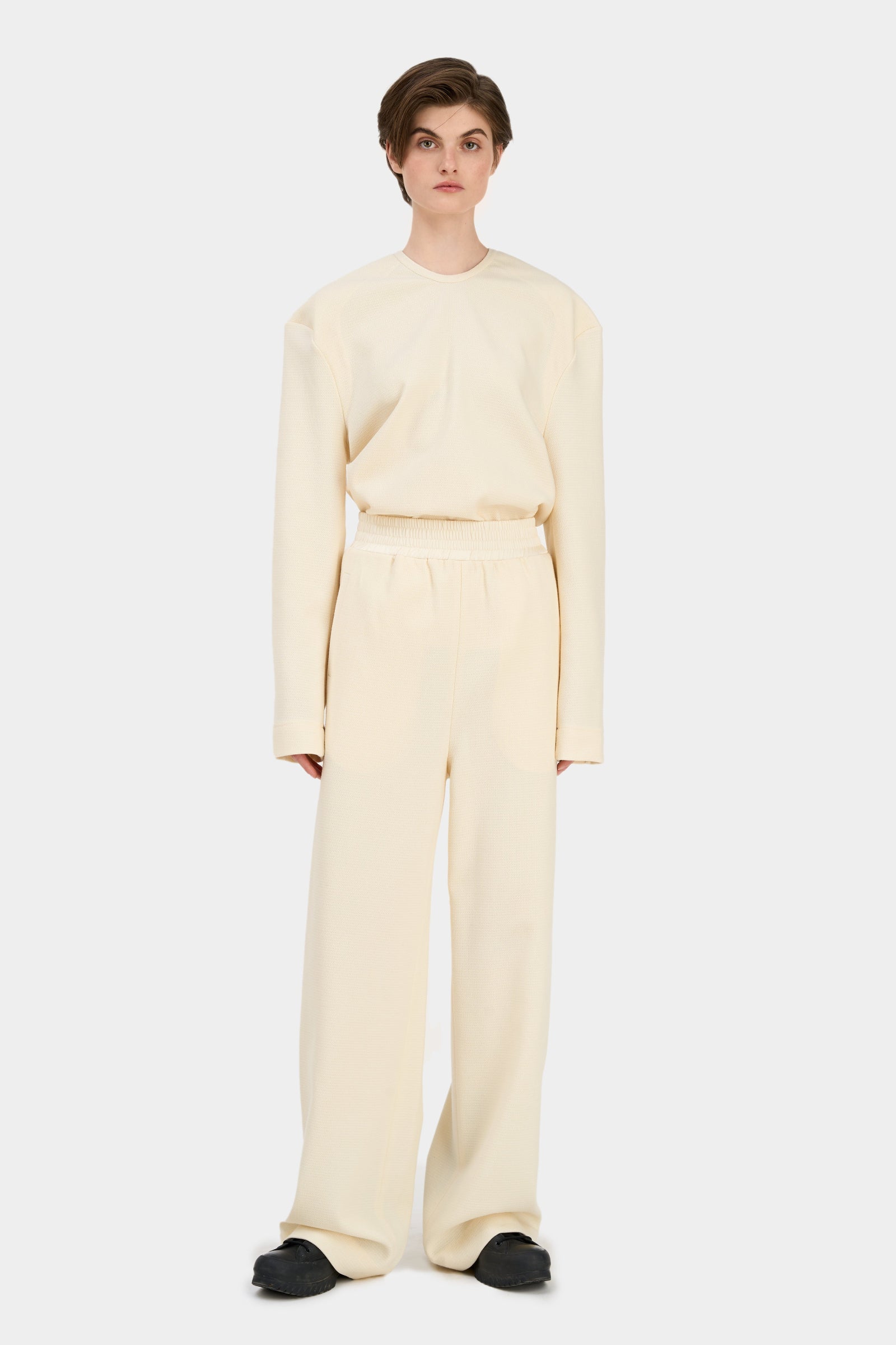 A model wearing loose-cut beige pants with an elastic waistband SOUL PANTS IVORY.
