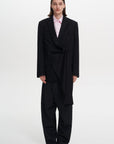 A model wearing a black, asymmetrically designed jacket TAG JACKET with a mandarin collar and long sleeves.