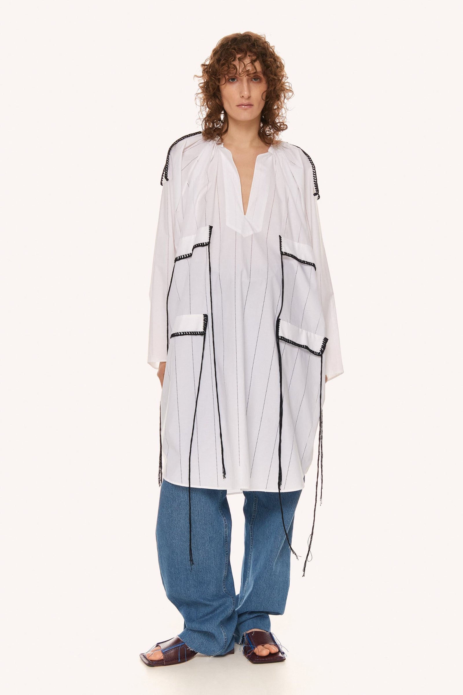 This image features a minimalist white dress with distinctive black detailing, presenting a modern and elegant aesthetic. The WHITE OBERIH DRESS dress is crafted from 100% cotton, highlighting both comfort and sustainability.