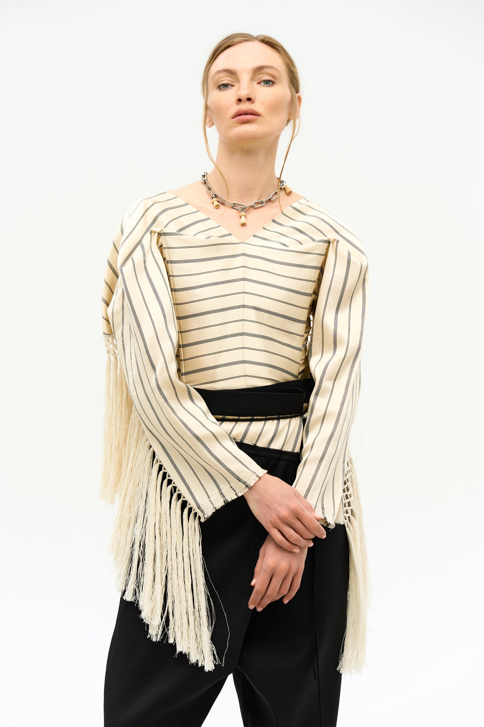 A model wearing a beige and black striped corset top  SVITA CORSET with long fringe detailing, paired with black trousers.